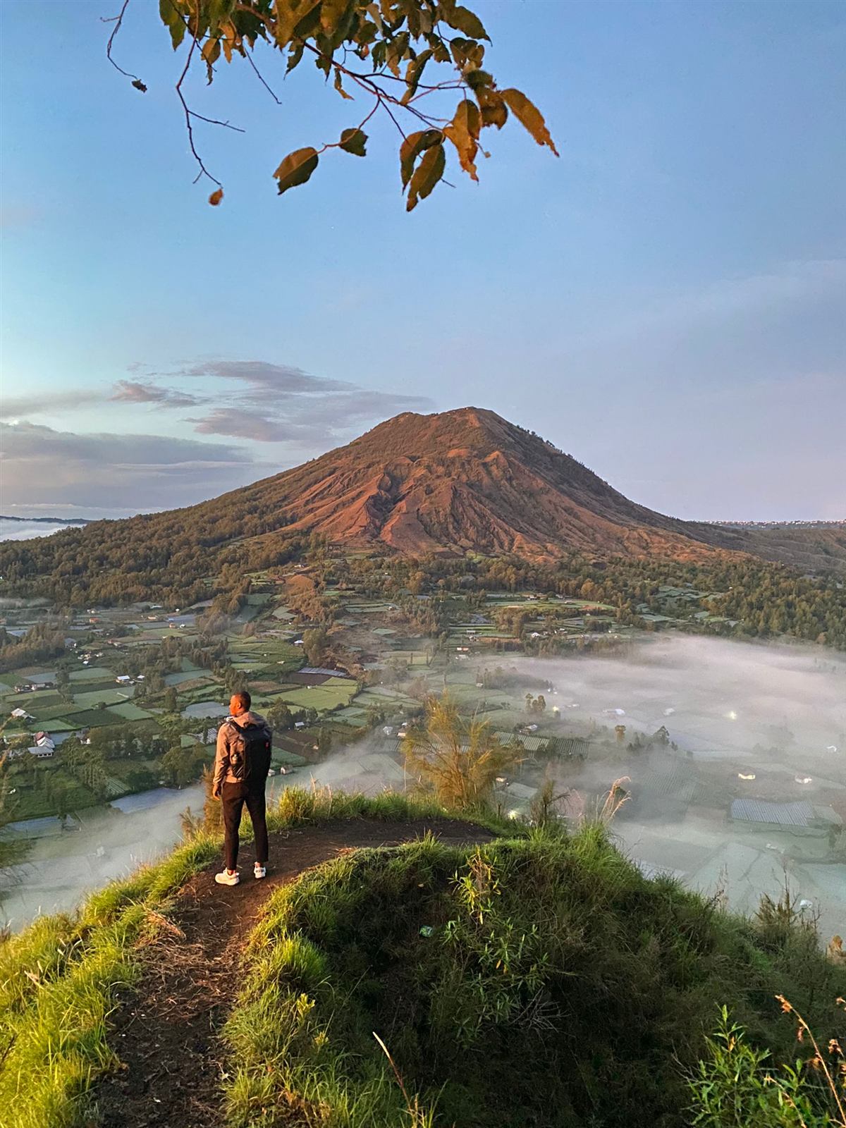 Mwata on a green ridge in Bali, looking out over a volcano rising above the morning mist.