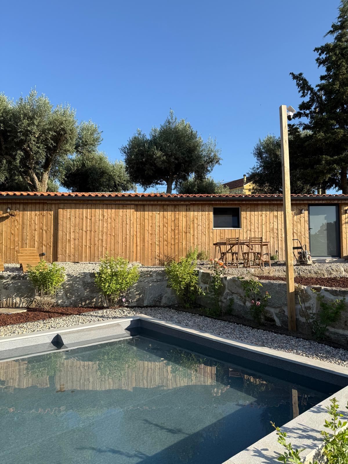 A timber cabin with a terracotta roof behind a small pool, with olive trees.