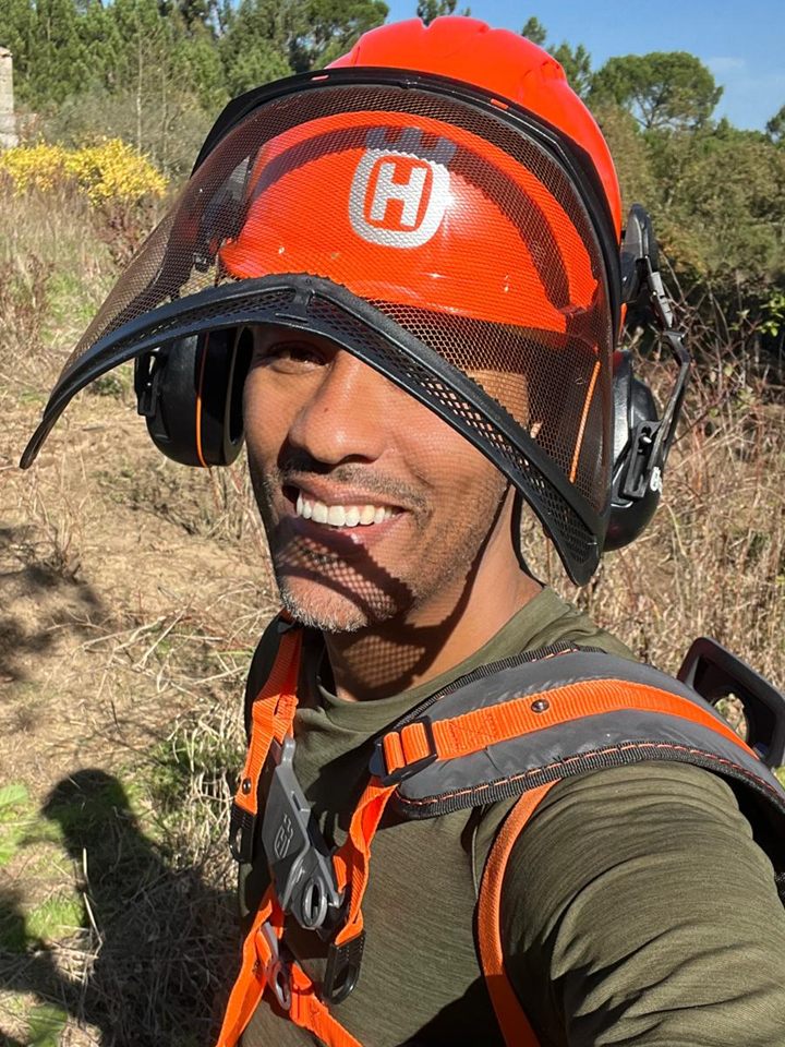 Mwata smiling in a safety helmet and visor, clearing brush on his land in Portugal.